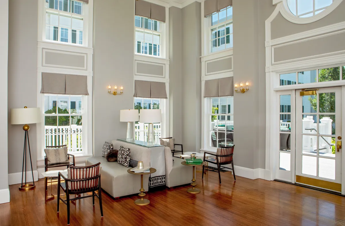 A spacious, tranquil interior featuring large windows that let in natural light, a modern seating arrangement with plush armchairs and an elegant coffee table, accented by decorative light fixtures. The scene feels bright and welcoming, with tasteful decor that reflects both comfort and style.