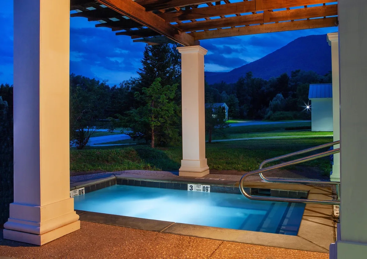 This image features an illuminated swimming pool beside a sleek pergola, set against a dramatic mountain backdrop. The tranquil ambiance invites relaxation, with soft lighting reflecting on the water, suggesting both daytime and evening enjoyment. The spacious pool area hints at the resort's luxury amenities available to guests.